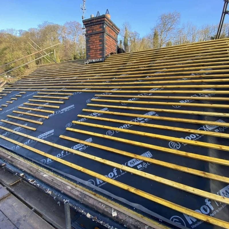 Roofing battens fitted over new underlay ahead of tiling, with the chimney stack exposed