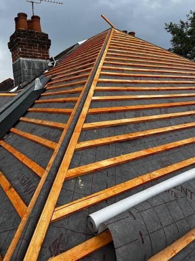 New timber battens fitted over roofing felt underlay, with chimney pots visible on the ridge